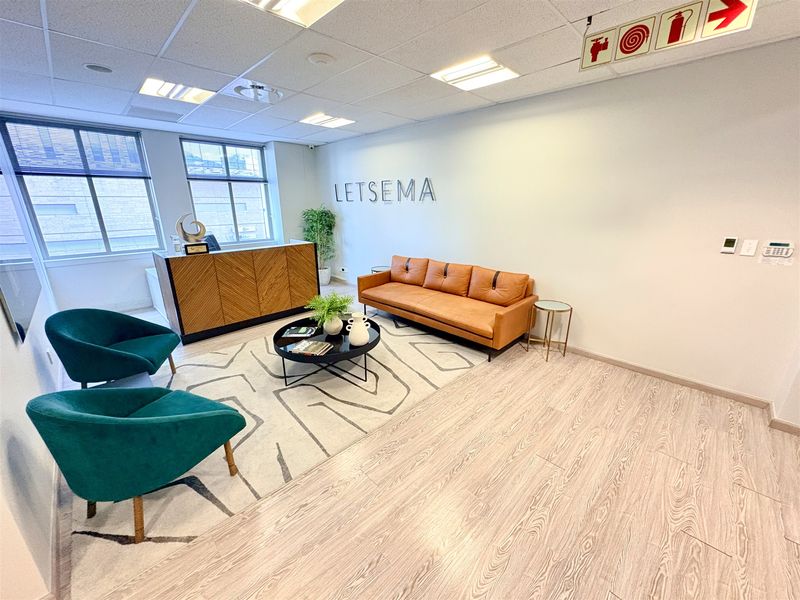 A professional office reception area featuring modern laminate flooring, a suspended ceiling with recessed lighting, and clear fire safety signage.