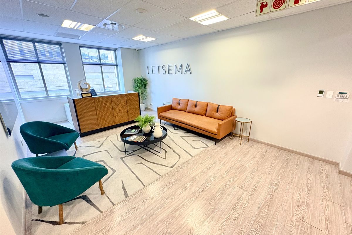 A professional office reception area featuring modern laminate flooring, a suspended ceiling with recessed lighting, and clear fire safety signage.