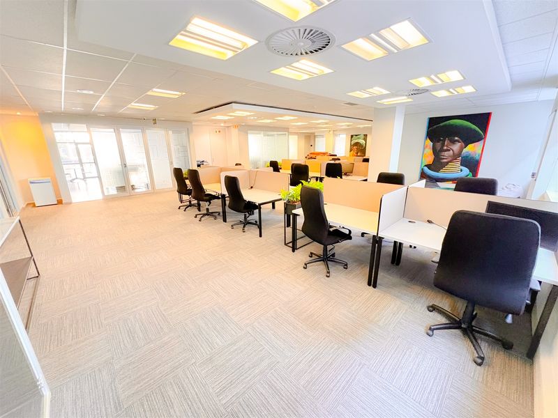 A well-lit open-plan office space featuring carpet tiles, recessed ceiling lighting, and glass partition doors, providing a professional and functional work environment.