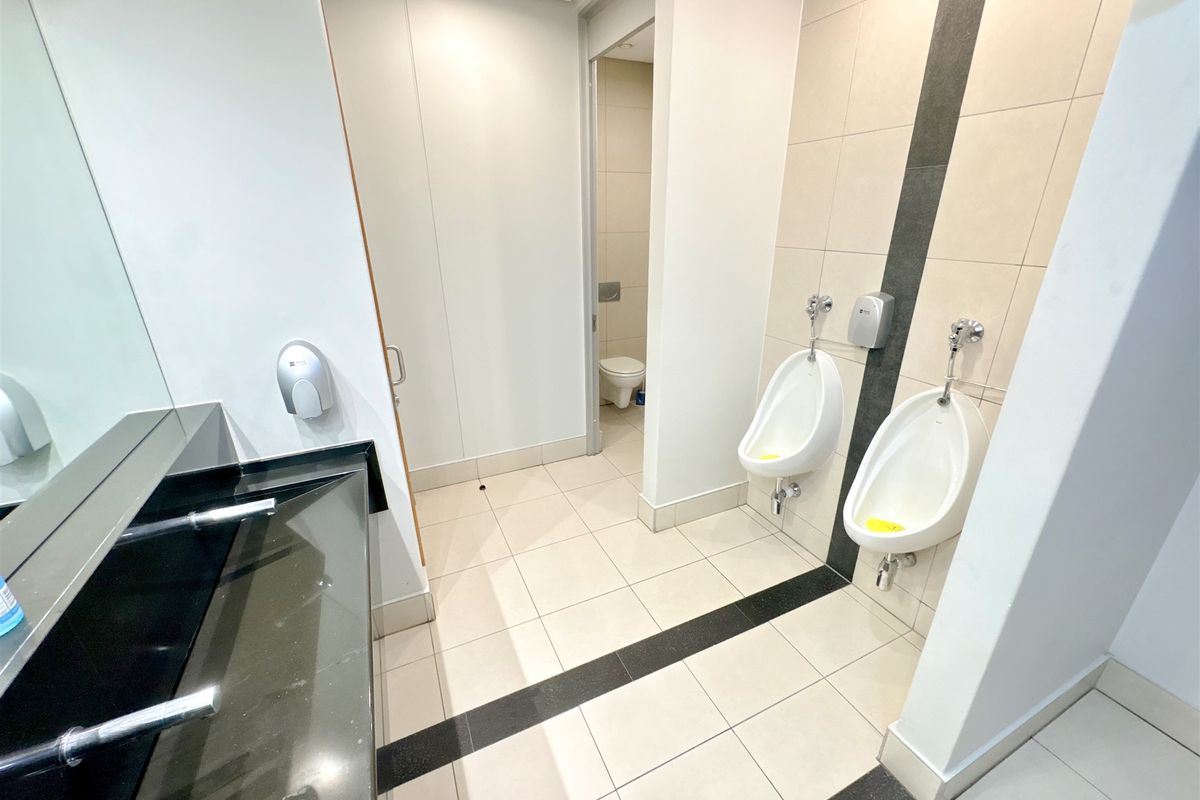 Modern commercial office bathroom featuring wall-mounted urinals, a stone vanity countertop, and neutral ceramic tiling throughout.