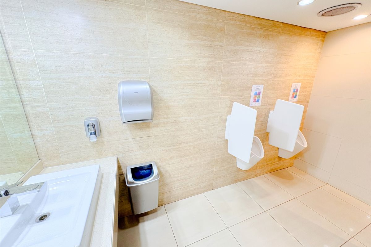 Modern office bathroom featuring wall-mounted urinals, a clean vanity basin, and neutral tiled finishes throughout.