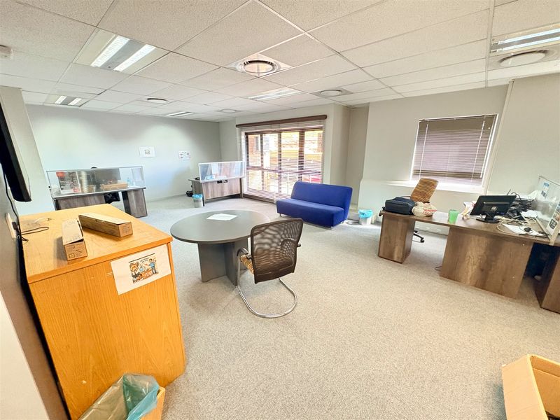 A spacious office area featuring a suspended ceiling, recessed lighting, and carpeted flooring, providing a functional workspace with natural light from large windows.