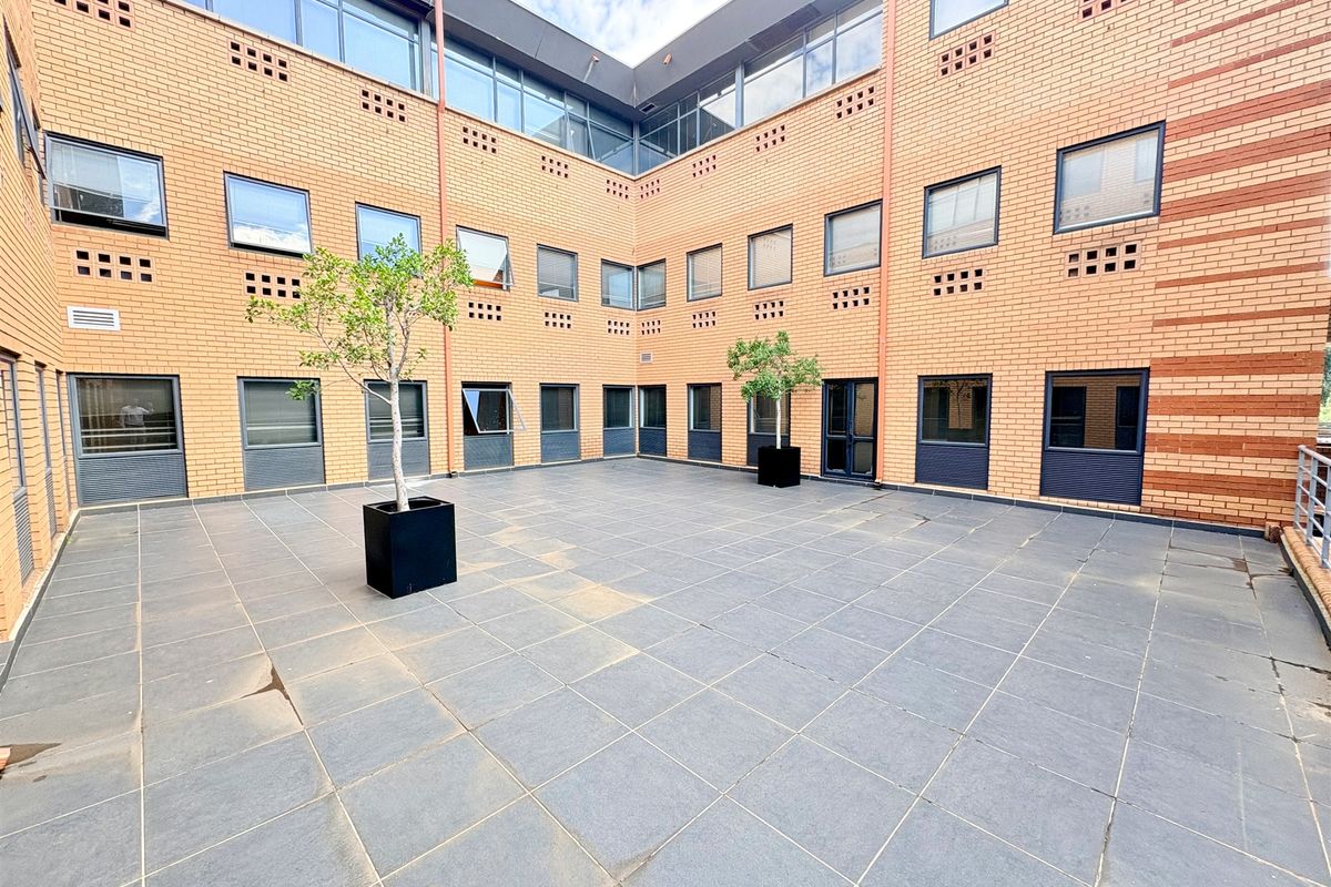 A spacious, paved central courtyard area surrounded by a multi-story brick office building with large windows and modern architectural detailing.