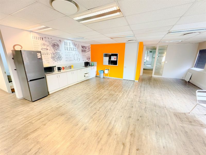A spacious office kitchenette featuring built-in cabinetry, laminate flooring, and a bright, open-plan layout suitable for staff break areas.