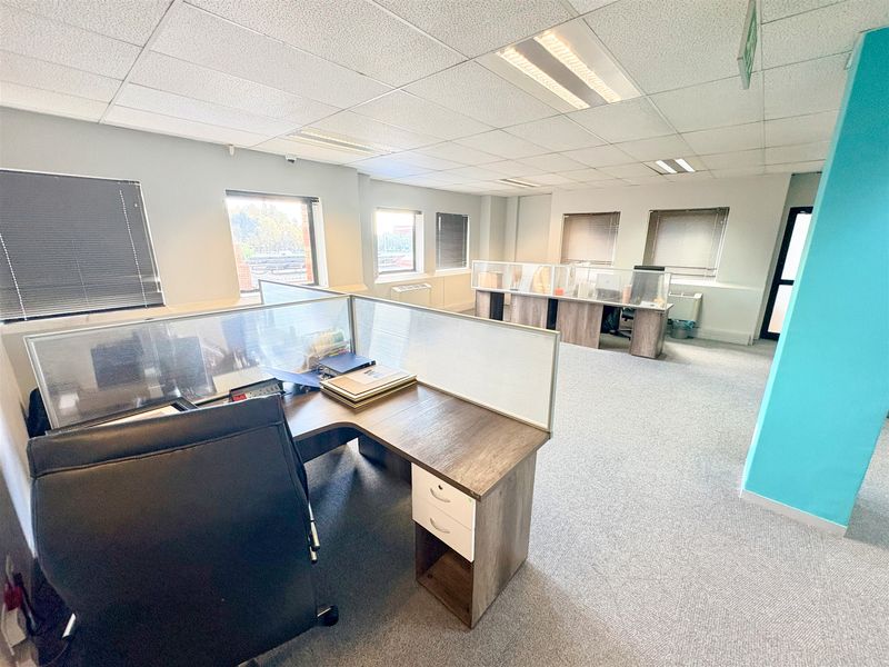 A functional open-plan office space featuring carpeted flooring, suspended ceilings with recessed lighting, and built-in workstation partitions with integrated blinds.