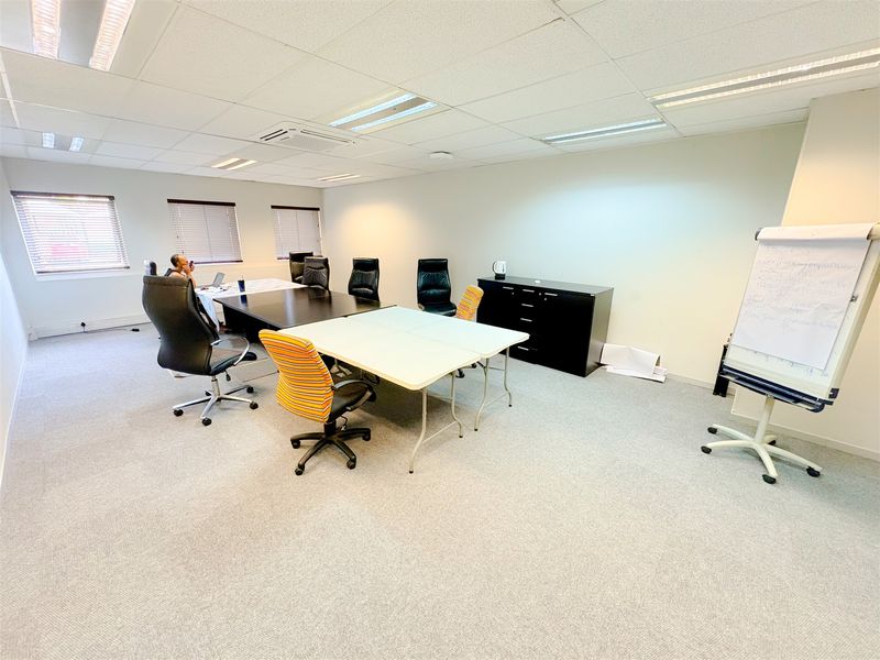 A functional office space featuring neutral carpeting, suspended ceiling tiles with recessed lighting, and multiple windows fitted with venetian blinds.
