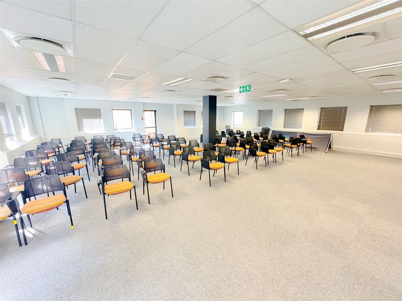 A spacious, open-plan office area featuring a suspended ceiling, recessed lighting, central air conditioning, and carpeted flooring, suitable for a conference or training room.