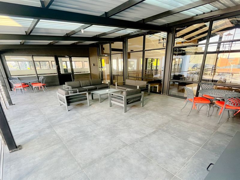 A spacious covered outdoor patio featuring large format floor tiles, a modern metal roof structure, and extensive glass facade panels.