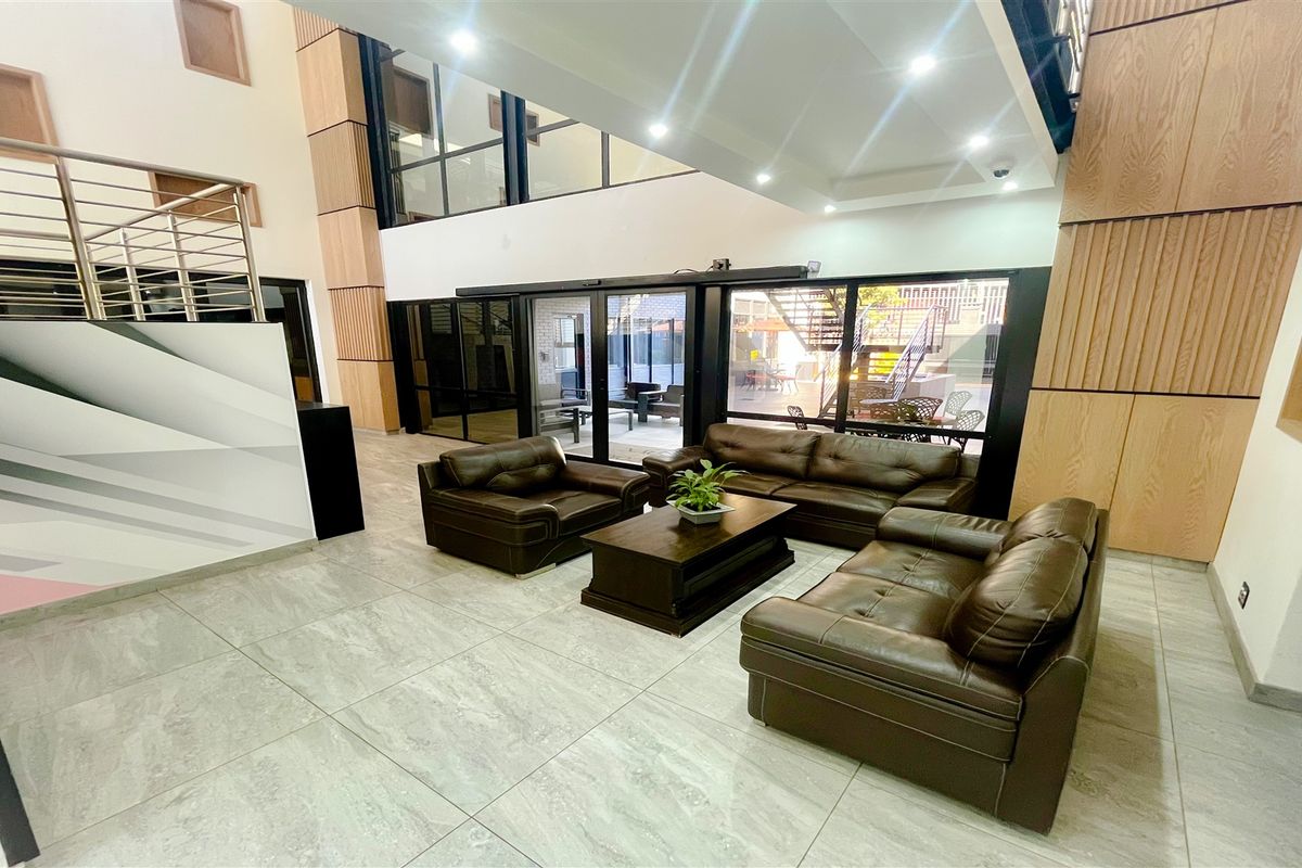 A spacious, modern double-volume office reception area featuring high ceilings, large sliding glass doors, contemporary tiled flooring, and elegant wood paneling accents.