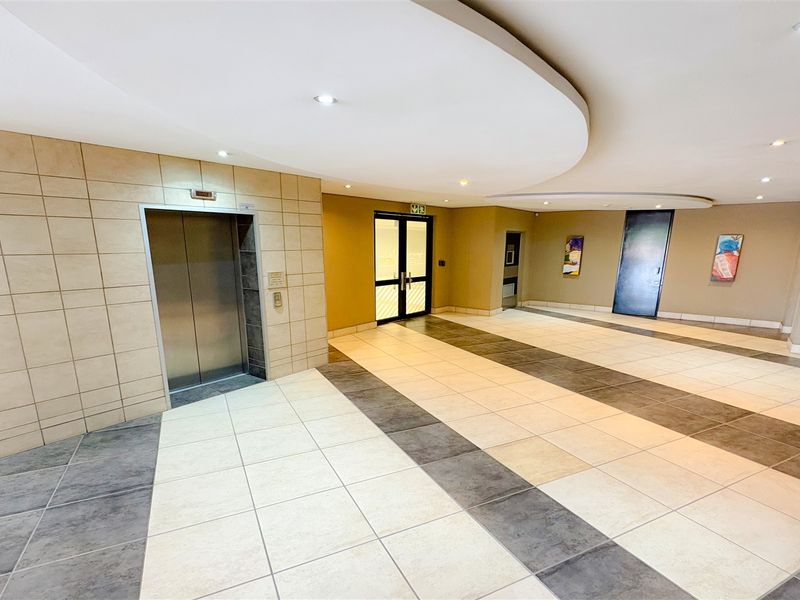 A spacious and modern office building lobby featuring tiled flooring, a central elevator, and recessed ceiling lighting.