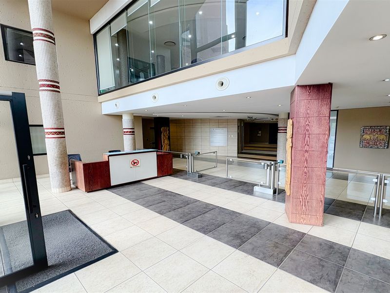 Spacious office building entrance lobby featuring a reception desk, security turnstiles, tiled flooring, and modern architectural detailing.