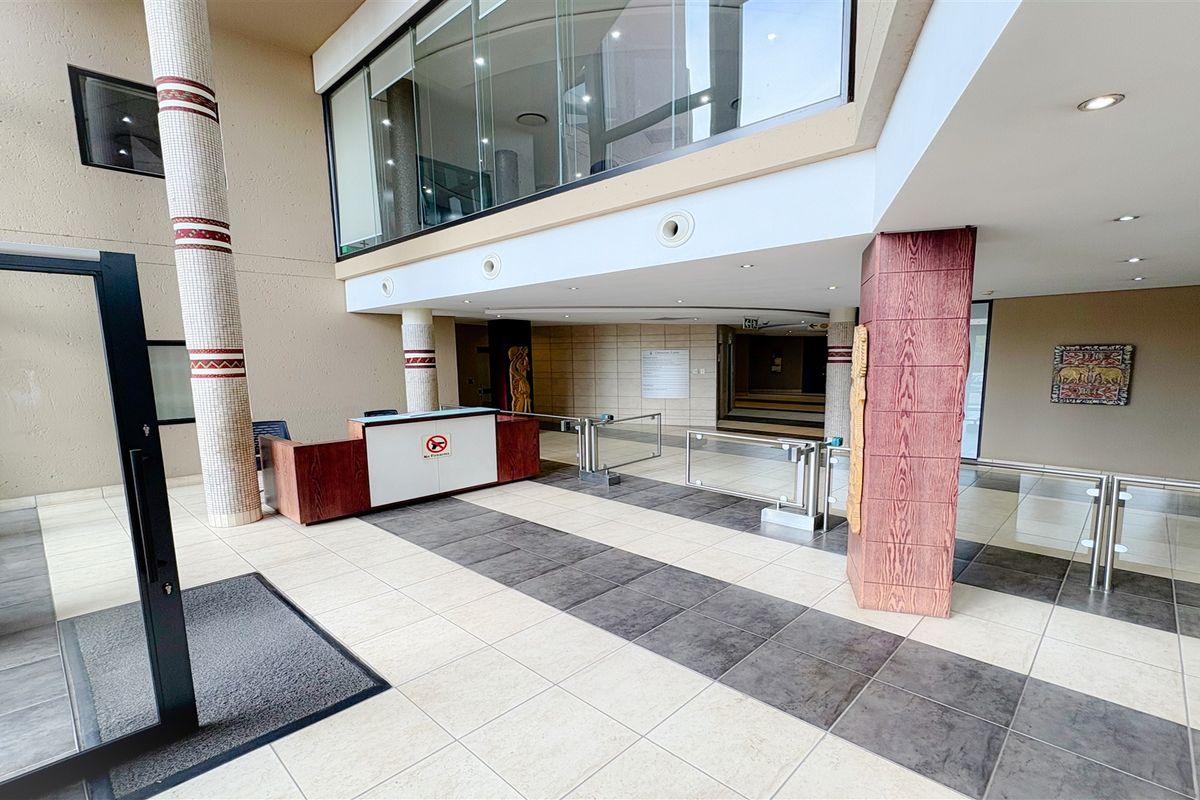 Spacious office building entrance lobby featuring a reception desk, security turnstiles, tiled flooring, and modern architectural detailing.