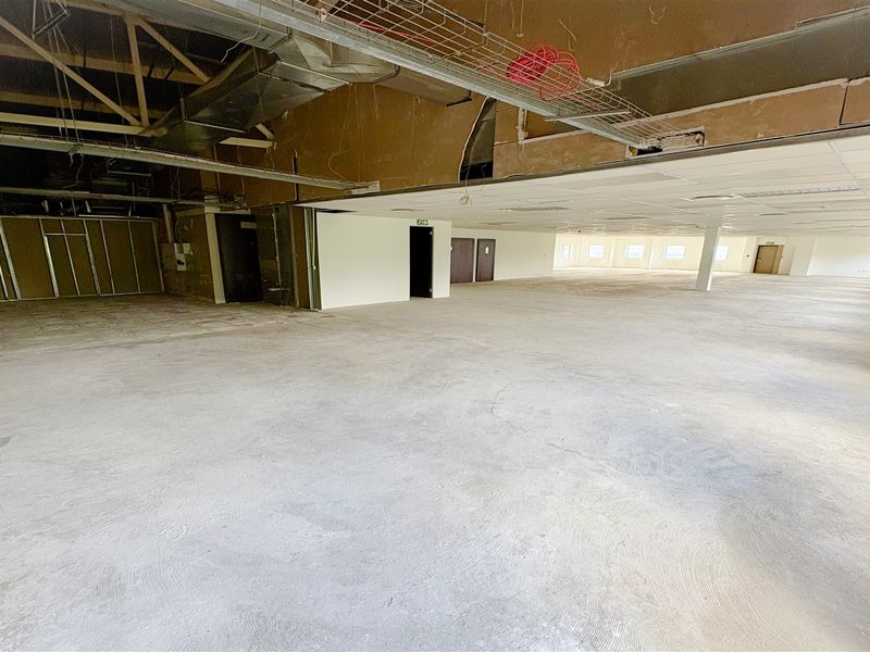 A large, open-plan office space in shell condition, featuring exposed ceiling infrastructure, concrete flooring, and unfinished wall partitions ready for custom fit-out.