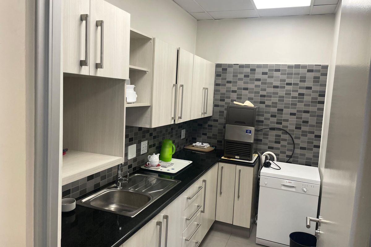 A functional office kitchenette featuring light wood-grain cabinetry, black granite countertops, a stainless steel sink, and a modern mosaic tile backsplash.