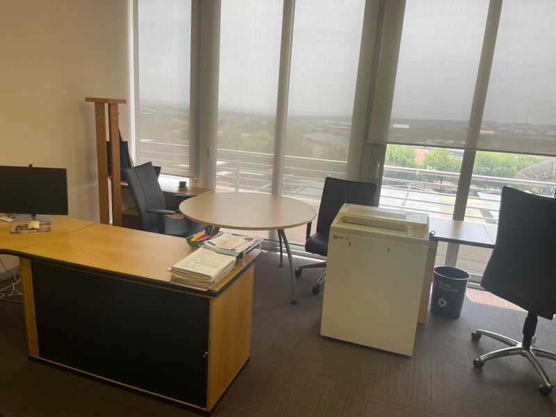 A functional office space featuring large floor-to-ceiling windows with roller blinds, providing ample natural light and an elevated view.