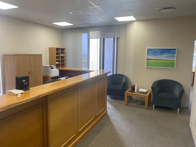 A professional office reception area featuring a built-in wooden reception desk, suspended ceiling tiles, and integrated lighting.