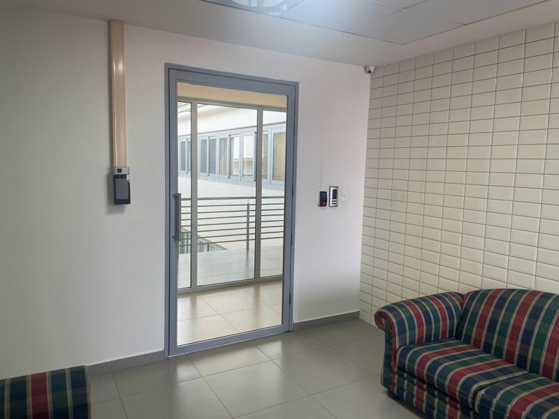 Office interior featuring a secure glass door with access control system, tiled feature wall, and neutral floor tiles.