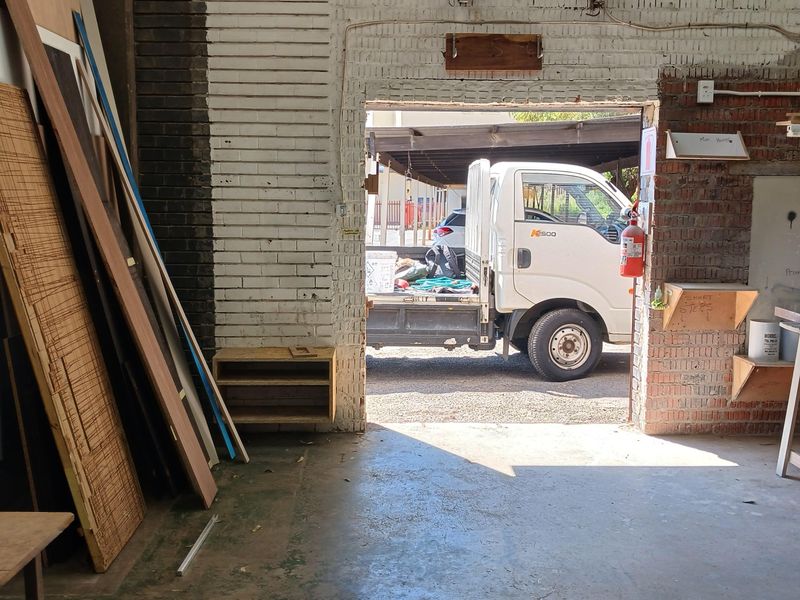 Industrial warehouse space featuring exposed brick walls, concrete flooring, and a large access opening for vehicle loading.
