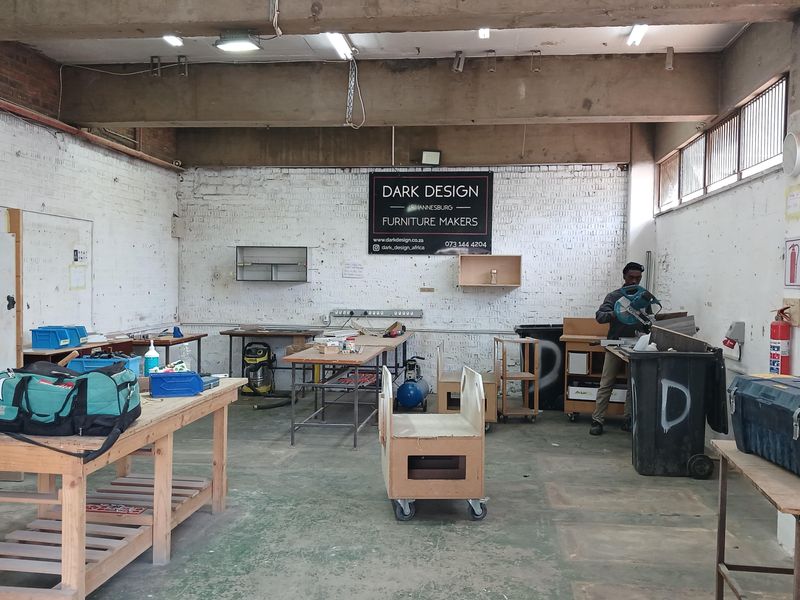 Industrial workshop space featuring high exposed concrete ceilings, painted brick walls, and durable concrete flooring, suitable for manufacturing or creative production use.