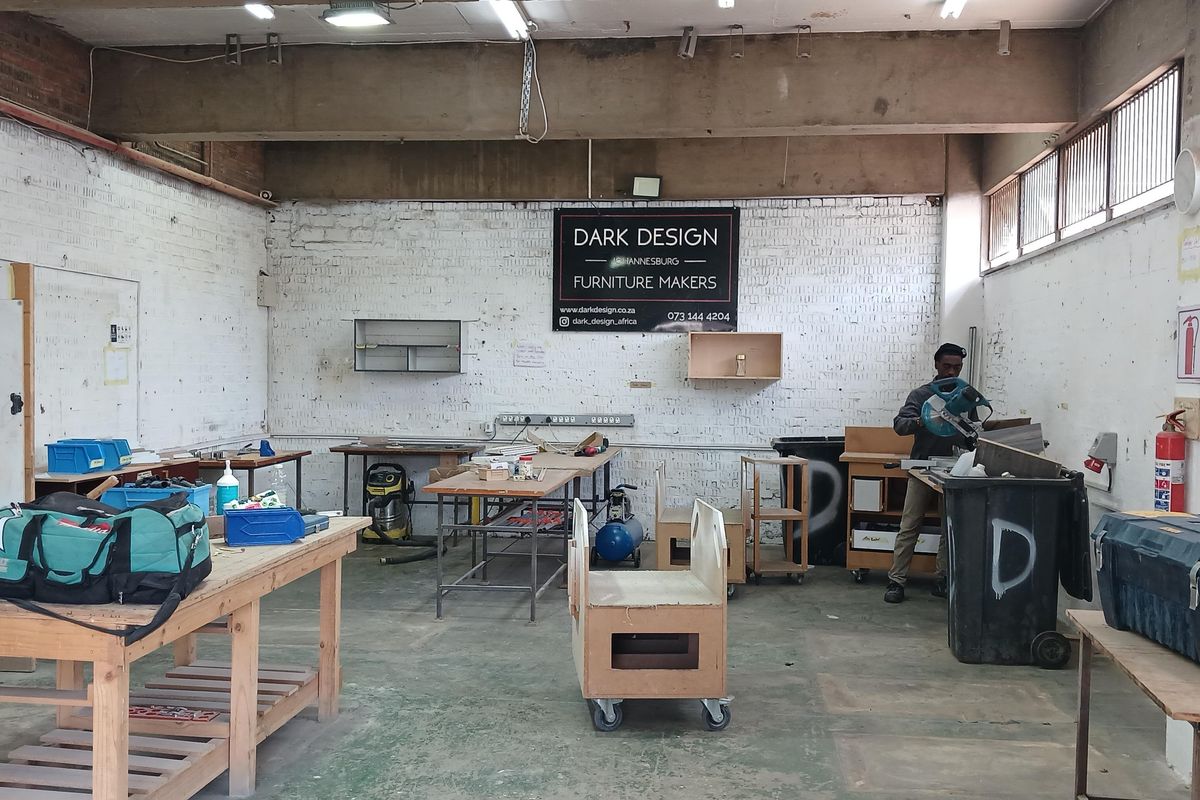 Industrial workshop space featuring high exposed concrete ceilings, painted brick walls, and durable concrete flooring, suitable for manufacturing or creative production use.
