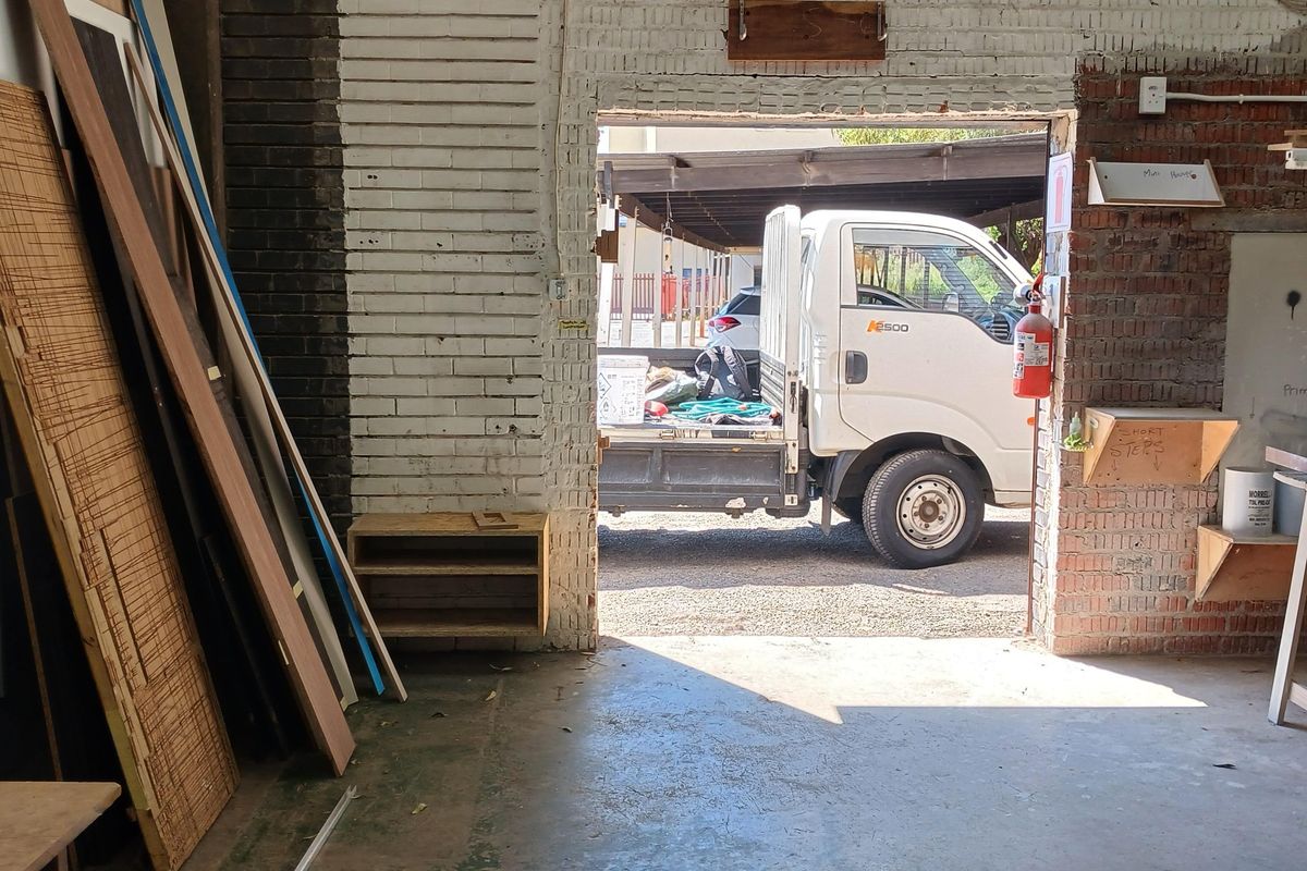 Industrial warehouse space featuring exposed brick walls, concrete flooring, and a large access opening for vehicle loading.