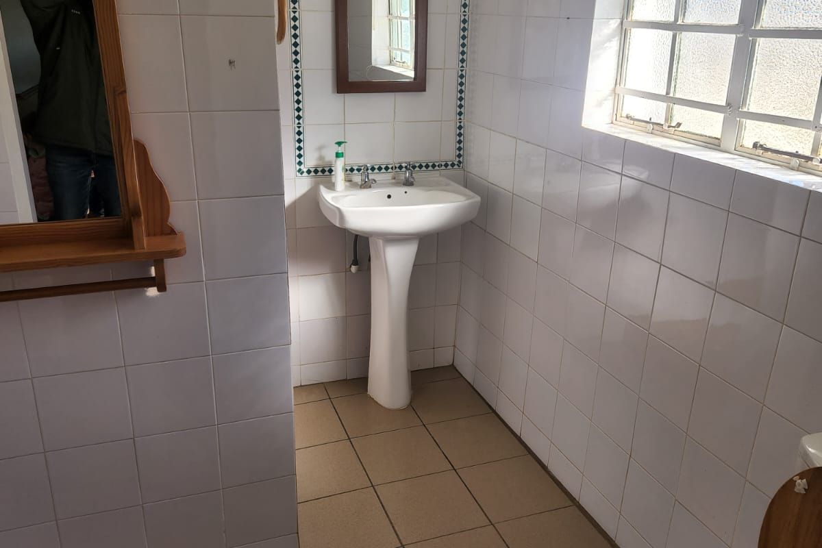 A functional bathroom featuring a pedestal basin, toilet, and tiled finishes, requiring some maintenance and cosmetic updates to improve its overall condition.