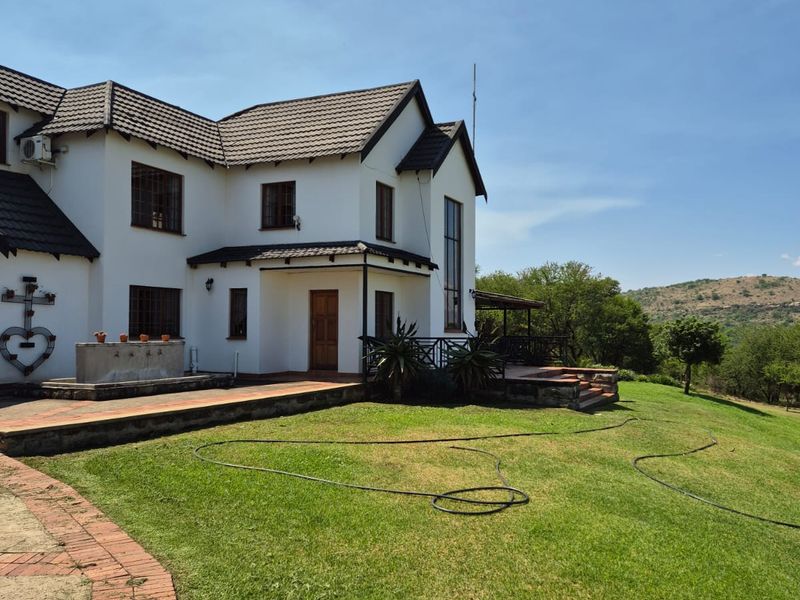 Rear view of a two-story farmhouse featuring a tiled roof, white exterior walls, a covered patio area, and a landscaped lawn with scenic views.