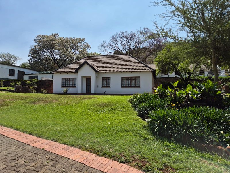 A well-maintained single-story farm residence featuring a tiled roof, timber window frames, and a spacious front lawn with established garden beds.
