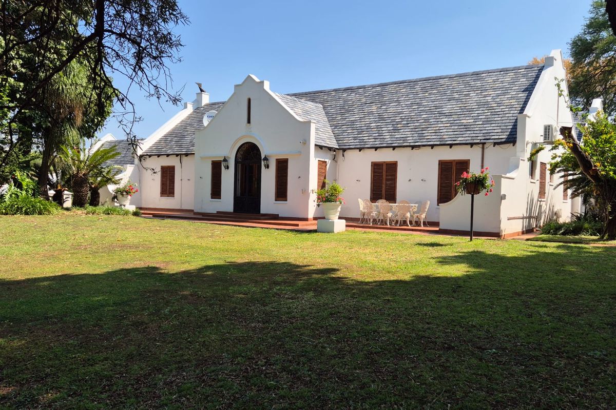 A charming farmhouse featuring a classic gabled roof, white exterior walls, and a spacious rear terrace overlooking a well-maintained garden.