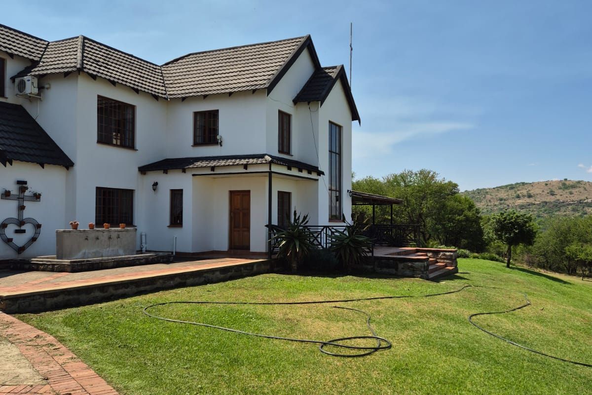 Rear view of a two-story farmhouse featuring a tiled roof, white exterior walls, a covered patio area, and a landscaped lawn with scenic views.