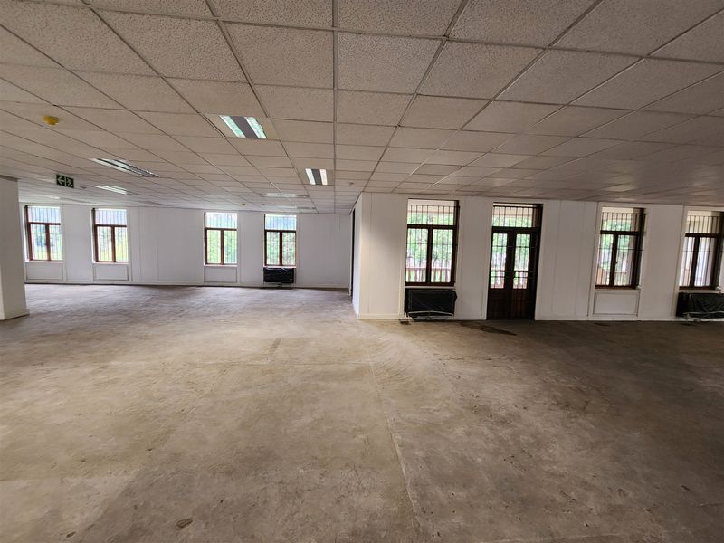 Spacious, open-plan office area featuring a suspended ceiling, recessed lighting, and large windows with security bars, offering a blank canvas for customization.