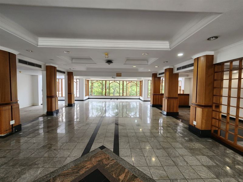 A spacious, open-plan office area featuring polished stone flooring, decorative wooden columns, and a coffered ceiling with integrated lighting and air conditioning.