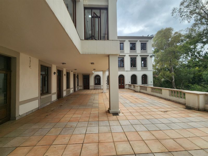 A spacious covered patio area featuring tiled flooring, structural concrete pillars, and a classic balustrade overlooking the surrounding grounds.