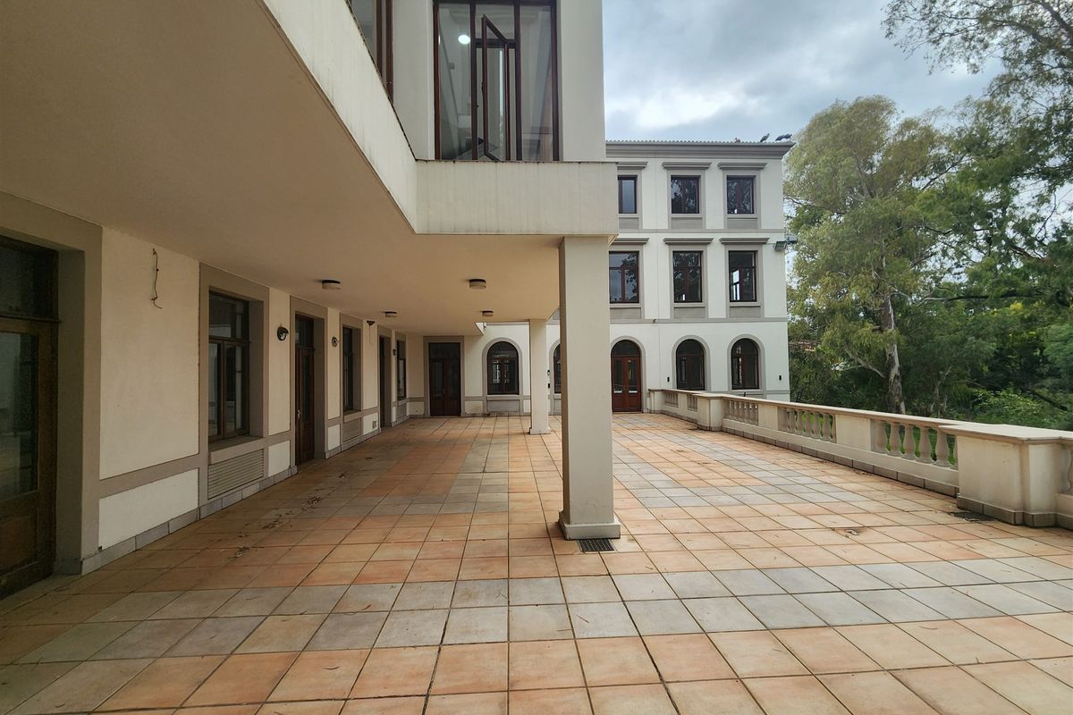 A spacious covered patio area featuring tiled flooring, structural concrete pillars, and a classic balustrade overlooking the surrounding grounds.