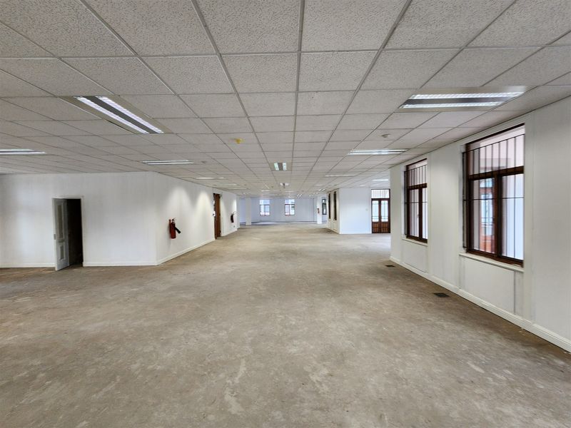 A large, open-plan office space featuring a suspended ceiling, recessed lighting, and security-barred windows, currently vacant and ready for custom fit-out.