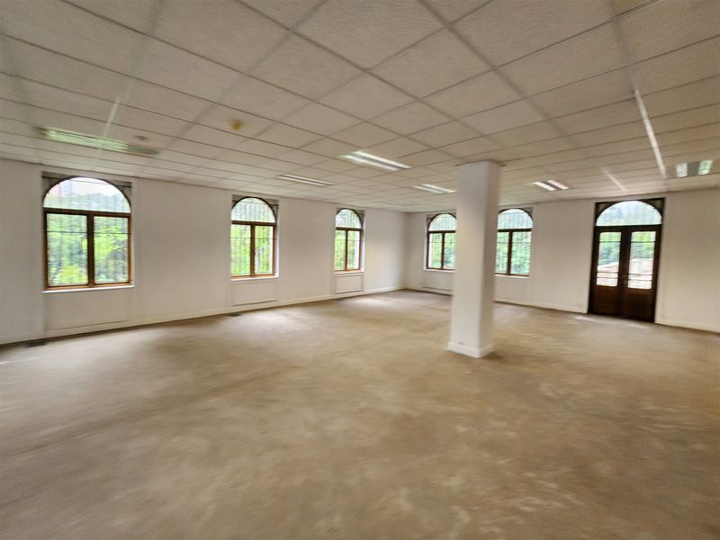 Spacious, open-plan office area featuring a suspended ceiling, recessed lighting, and multiple arched windows providing natural light.
