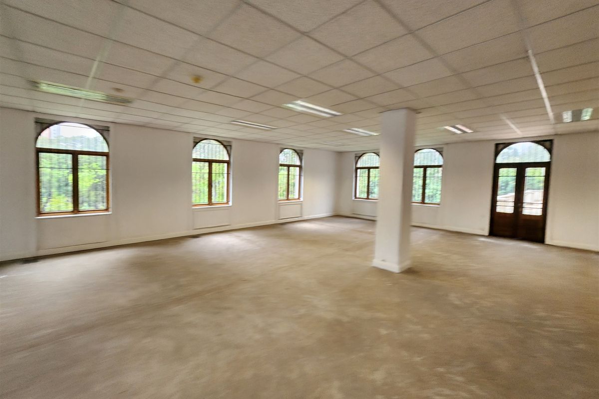 Spacious, open-plan office area featuring a suspended ceiling, recessed lighting, and multiple arched windows providing natural light.