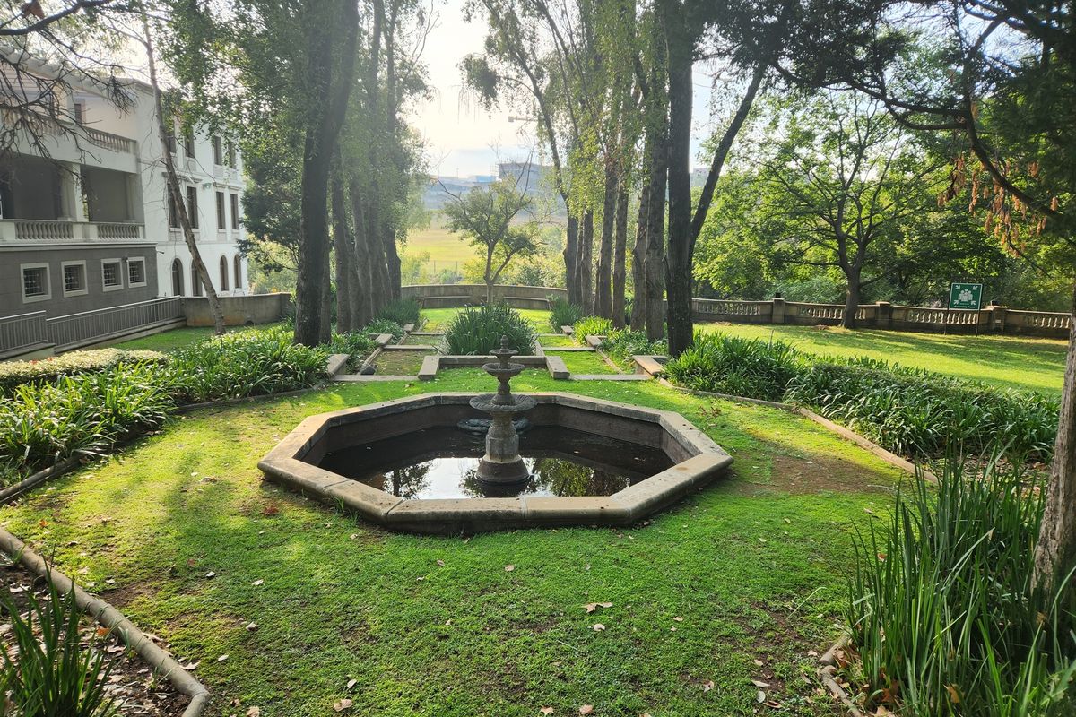 A well-maintained landscaped garden featuring a central stone fountain, mature trees, and stone balustrade detailing, providing a serene outdoor space.