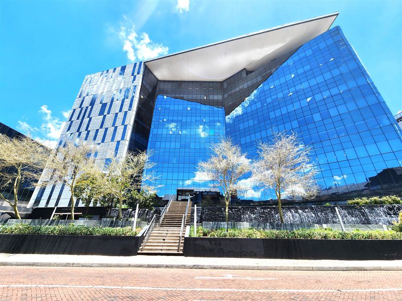 Modern commercial office building featuring a striking glass facade, prominent water feature, and grand stone staircase entrance.