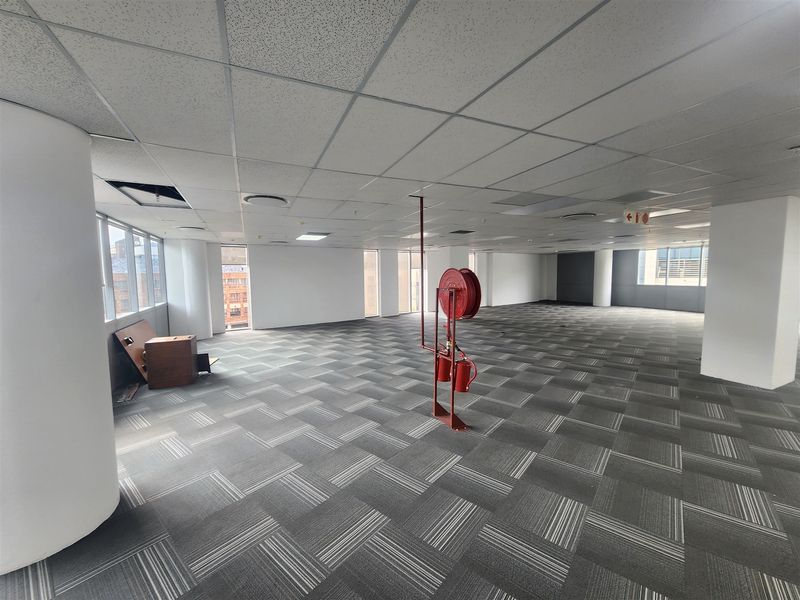 An open-plan office space featuring carpet tiles, a suspended ceiling, and integrated fire safety equipment, offering a versatile layout for professional use.