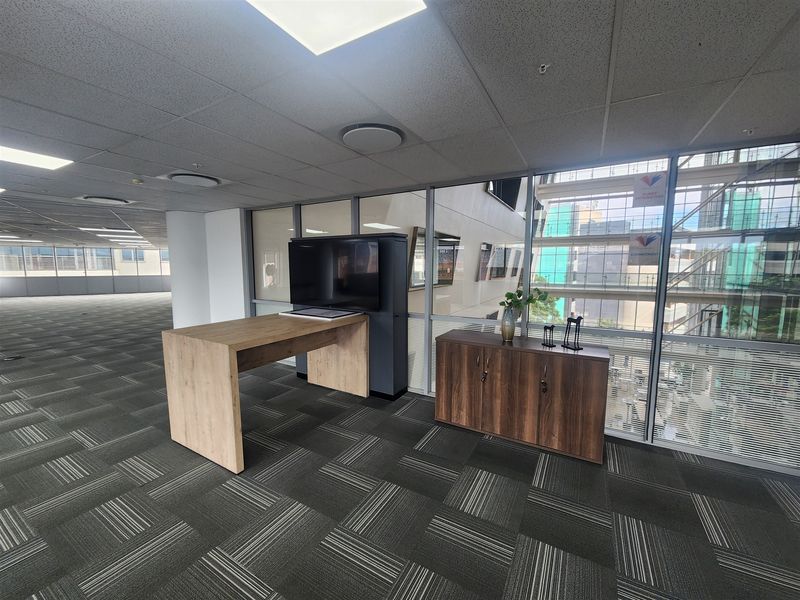 Open-plan office space featuring carpet tiles, suspended ceilings with recessed lighting, and extensive glass partitioning providing natural light and views.