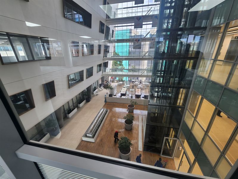 A modern multi-story office atrium featuring a glass elevator shaft, expansive curtain wall glazing, and high-quality interior finishes.