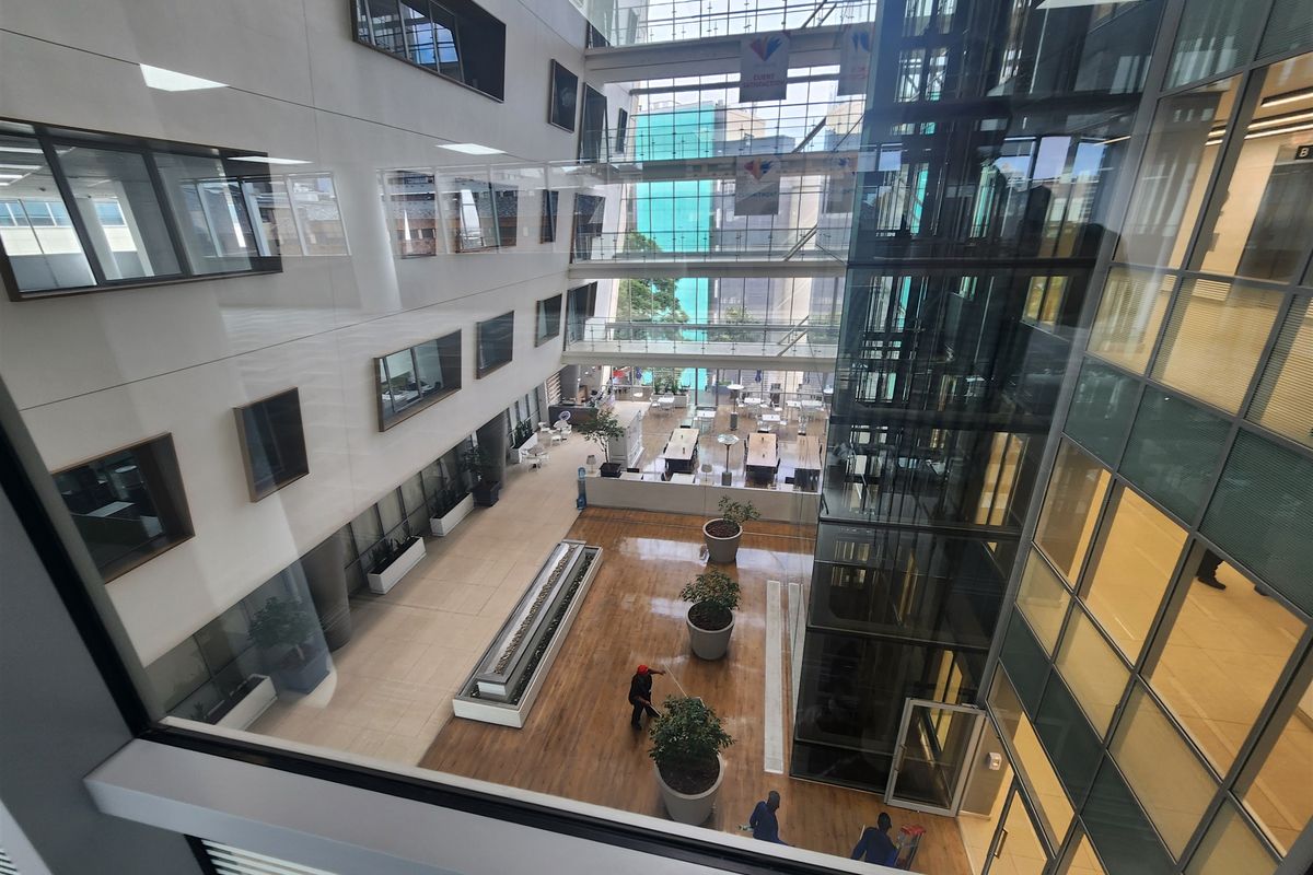 A modern multi-story office atrium featuring a glass elevator shaft, expansive curtain wall glazing, and high-quality interior finishes.