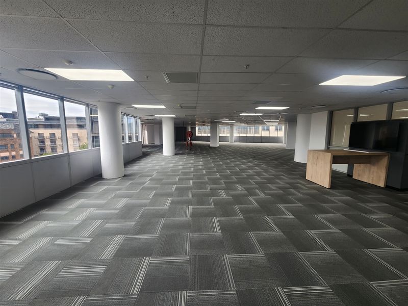 A spacious, open-plan office area featuring a suspended ceiling, recessed lighting, and carpet tiles, offering a bright and professional workspace environment.
