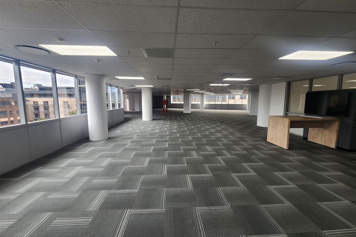 A spacious, open-plan office area featuring a suspended ceiling, recessed lighting, and carpet tiles, offering a bright and professional workspace environment.