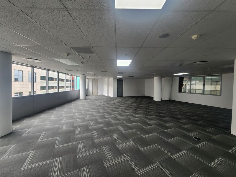 Spacious, open-plan office area featuring large windows, carpet tiles, and a suspended ceiling with integrated lighting, offering a clean and professional workspace.