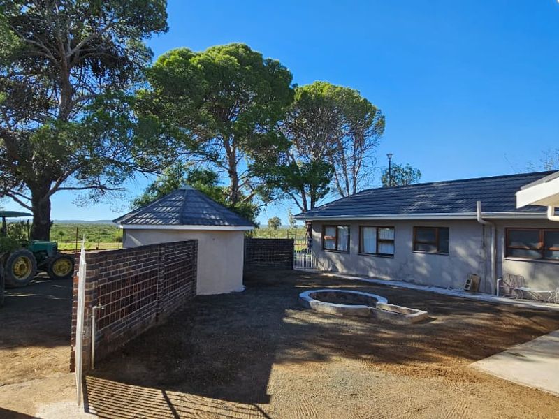 A rear exterior view of the farm property featuring a courtyard area, brick boundary wall, and surrounding mature trees.