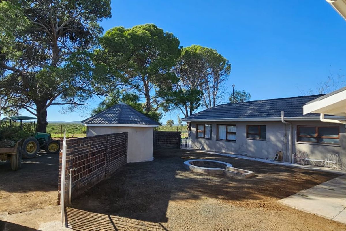 A rear exterior view of the farm property featuring a courtyard area, brick boundary wall, and surrounding mature trees.