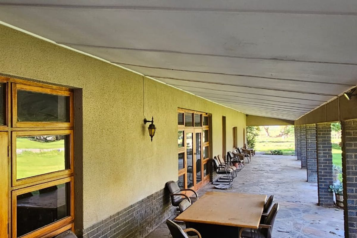 A spacious covered patio featuring stone flooring, brick support pillars, and large wooden-framed windows overlooking the surrounding farm landscape.