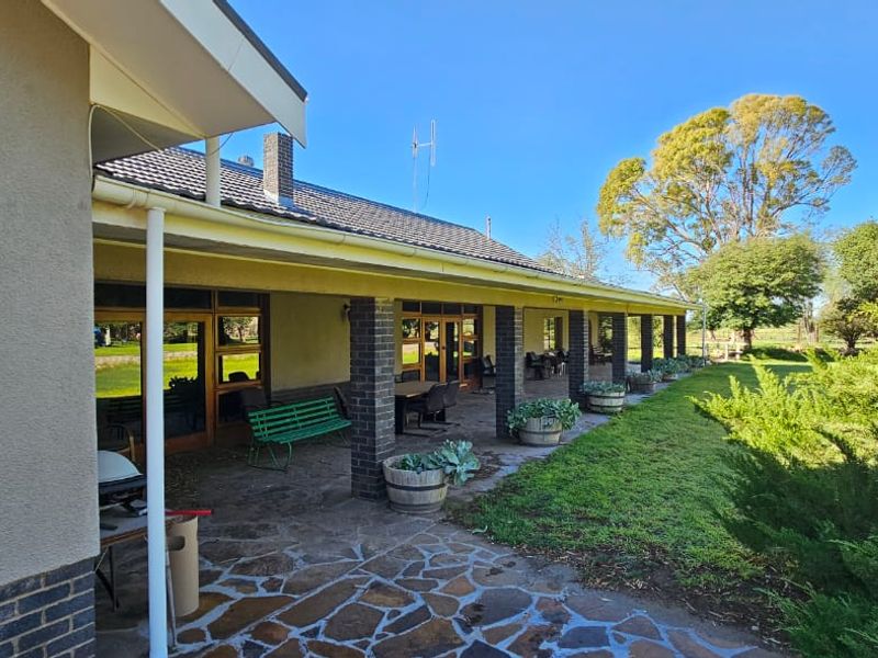 A spacious covered patio featuring stone paving, brick pillars, and direct access to the expansive garden and surrounding farm landscape.
